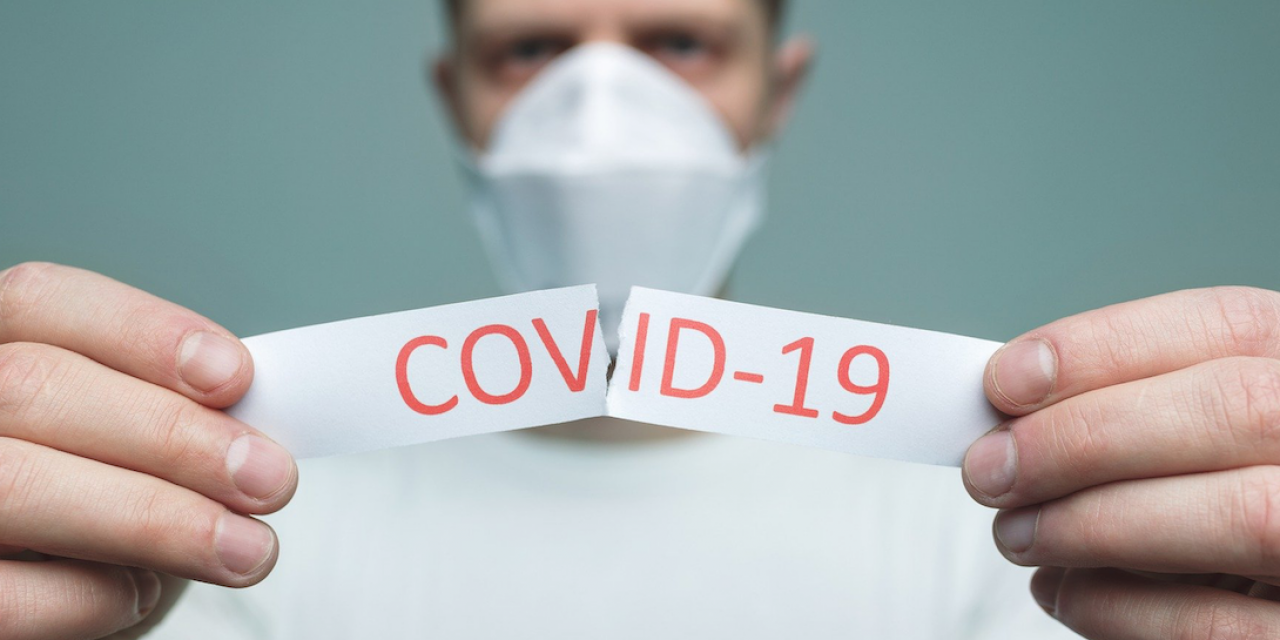 Un homme avec un masque qui déchire un papier contenant le mot COVID-19