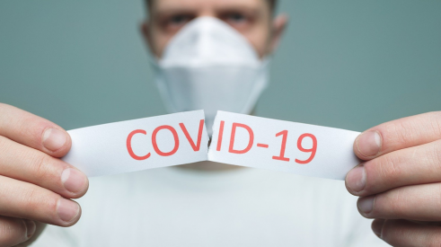 Un homme avec un masque qui déchire un papier contenant le mot COVID-19